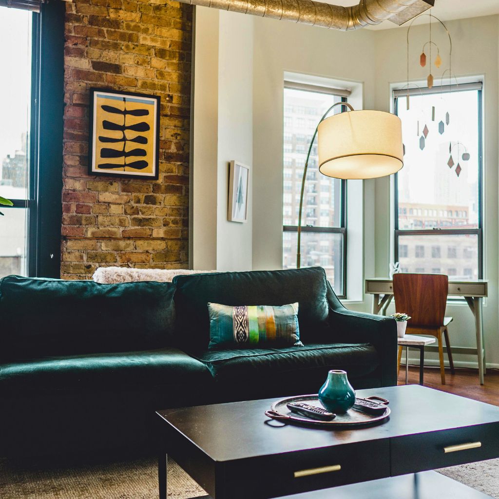 A living room with a green sofa, three windows and a lampshade